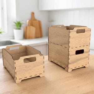 Peut inclure: Deux boîtes de rangement en bois avec une finition claire veinée, posées sur une surface en bois. L'une est ouverte, l'autre est empilée avec une ouverture rectangulaire. Les deux ont des découpes pour les poignées.