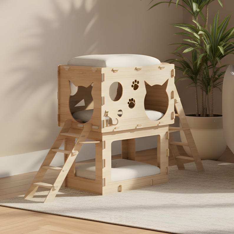 Puede incluir: Una casa para gatos de madera de dos pisos con un acabado claro. La estructura presenta formas de gato recortadas, huellas de patas y una silueta de gato. Cada nivel tiene un coj&iacute;n blanco. Dos peque&ntilde;as escaleras de madera dan acceso a cada nivel.