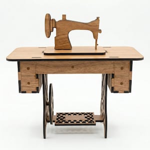 K&ouml;nnte beinhalten: Eine Miniatur-N&auml;hmaschine aus Holz mit Tisch und Schubladen. Die N&auml;hmaschine ist braun und hat ein gro&szlig;es Rad an der Seite. Der Tisch hat eine hellbraune Oberfl&auml;che und verf&uuml;gt &uuml;ber zwei Schubladen auf jeder Seite. Die Beine sind schwarz.