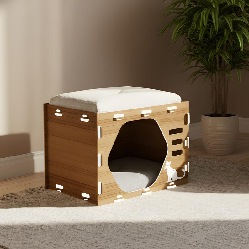 Puede incluir: Una casa para gatos de madera con un coj&iacute;n de color claro en la parte superior. La casa para gatos tiene una abertura hexagonal y un coj&iacute;n gris en el interior. Una silueta de gato blanco est&aacute; en el lateral. La casa es de madera marr&oacute;n claro.