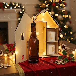 Könnte beinhalten: Ein holzförmiges Haus-Display mit einer braunen Bierflasche und zwei weißen Tassen. Das Display wird von einer Lichterkette beleuchtet und steht auf einem roten Samtläufer mit Weihnachtsdekorationen. Eine festliche Urlaubsszene.