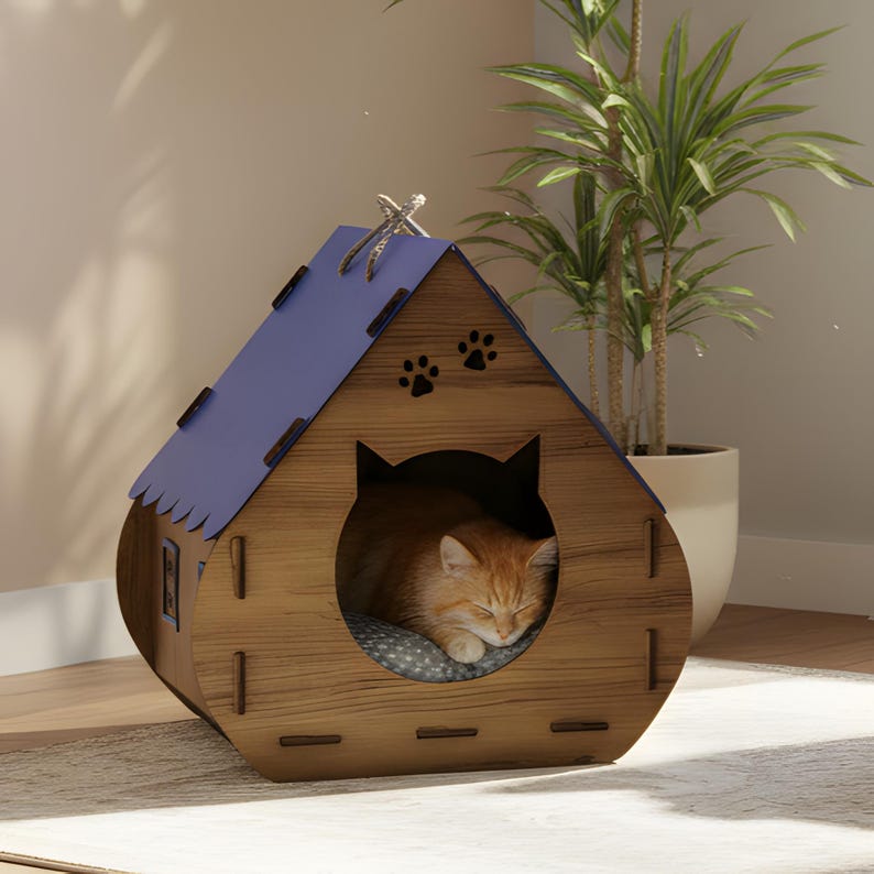 Puede incluir: Una casa para gatos de madera con techo azul y entrada en forma de gato. La casa tiene recortes de huellas de patas y un gato atigrado naranja durmiendo dentro sobre un coj&iacute;n gris. La casa es de madera y tiene un acabado natural.