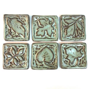 May include: Six ceramic tiles with different leaf designs in shades of green and brown. The tiles are square and have a textured surface.