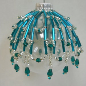 May include: A clear glass Christmas ornament with a teal and silver beaded design. The ornament has a silver hanger and a beaded fringe.
