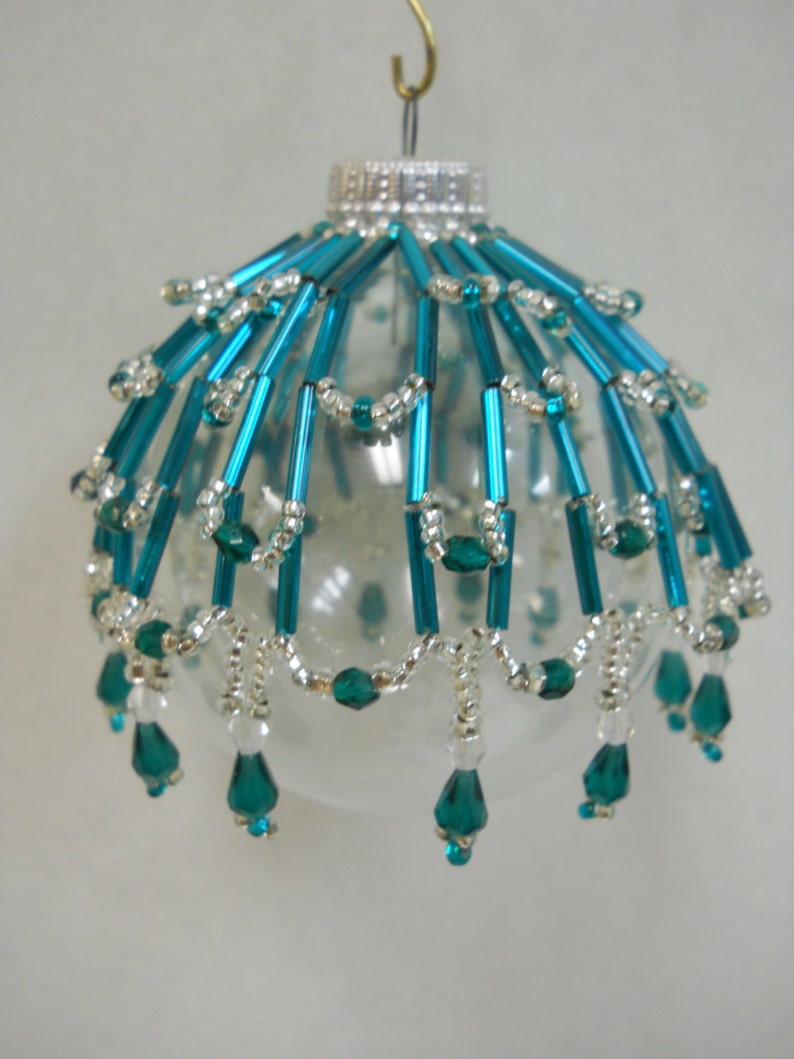 May include: A clear glass Christmas ornament with a teal and silver beaded design. The ornament has a silver hanger and a beaded fringe.