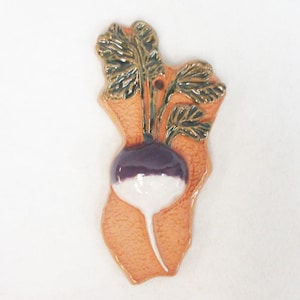 May include: A ceramic ornament shaped like a turnip with a purple top and white bottom. The turnip has green leaves and is on a light orange background.