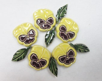 May include: Six yellow ceramic pansies with purple centers and green leaves. The pansies are arranged in a circle.