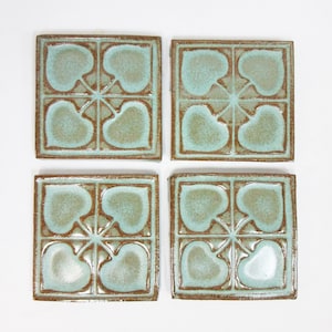 May include: Set of four square ceramic tiles with a light blue glaze and a brown border. Each tile features a design of four stylized leaves in a repeating pattern.