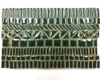 Puede incluir: Una colección de azulejos de cerámica de color verde bosque oscuro dispuestos en una cuadrícula rectangular. Los azulejos presentan varias formas, incluyendo cuadrados pequeños, rectángulos delgados y triángulos, todos con un acabado brillante y reflejos de luz visibles.
