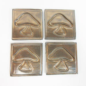 May include: Four square ceramic tiles with a raised mushroom design. The tiles are a dark brown color with a metallic sheen.
