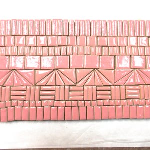 May include: A mosaic tile design in shades of pink. The tiles are arranged in a rectangular pattern, featuring squares, rectangles, and triangular shapes. The design has a geometric, art deco style.