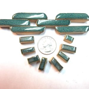 May include: A collection of small, rectangular ceramic tiles in varying sizes. The tiles have a teal glaze with a textured surface and are arranged around a US quarter. The tiles are likely for a mosaic or craft project.