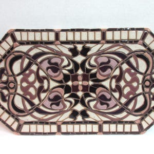 May include: Octagonal ceramic tile mosaic features an Art Nouveau design. The mosaic is predominantly off-white with dark burgundy and mauve accents. The design is symmetrical and features stylized floral motifs and flowing lines. The tile is framed by a border of smaller, off-white and burgundy tiles. This decorative tile is suitable for various applications, including tabletops, wall art, or flooring.