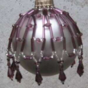 May include: A silver Christmas ornament with a purple beaded trim. The beads are arranged in a cascading pattern, creating a festive and elegant look.