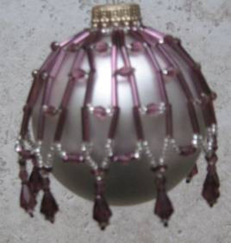 May include: A silver Christmas ornament with a purple beaded trim. The beads are arranged in a cascading pattern, creating a festive and elegant look.