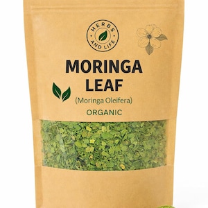 May include: A brown paper bag with a clear window showing dried green moringa leaves. The bag has the text "MORINGA LEAF" and "ORGANIC", plus a circular logo reading "HERBS AND LIFE". A flower graphic is also visible.