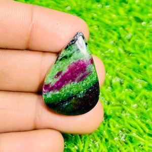 May include: A teardrop-shaped gemstone with a vibrant mix of colors. The stone features a striking combination of deep green, rich magenta, and black hues, creating a unique and eye-catching appearance. The polished surface reflects light.