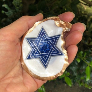 May include: A white seashell with a gold rim, featuring a blue and silver Star of David design.
