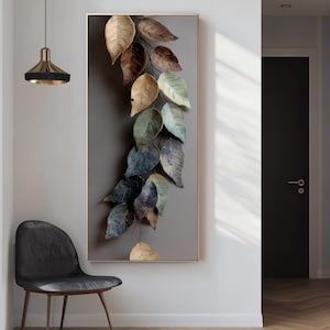 Może przedstawiać: Oprawione dzieło sztuki przedstawiające kaskadę stylizowanych liści w odcieniach brązu, złota i niebiesko-zielonego. Liście ułożone są na szarym tle w złotej ramie, tworząc naturalną, a zarazem nowoczesną estetykę.