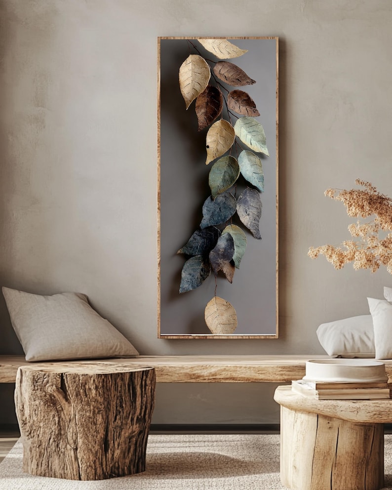 Op de afbeelding: Een rechthoekig wandkunstwerk met een houten frame, met een rank van gestileerde bladeren in goud, bruin en blauwgroen. De bladeren zijn geplaatst tegen een grijze achtergrond, wat een natuurlijke esthetiek cre&euml;ert. Het kunstwerk wordt tentoongesteld in een neutraal getinte woonruimte.