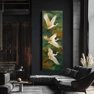 May include: A vertical canvas art piece featuring three white cranes in flight against a green and gold background. The birds have outstretched wings and long, curved necks. The artwork is displayed in a modern living room setting.