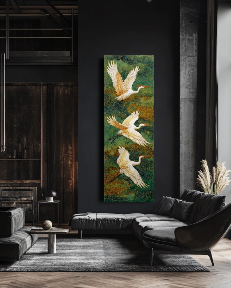 May include: A vertical canvas art piece featuring three white cranes in flight against a green and gold background. The birds have outstretched wings and long, curved necks. The artwork is displayed in a modern living room setting.