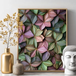 May include: A framed floral print with a gold frame, featuring a close-up of overlapping, multi-colored leaves in shades of green, pink, and purple. A gold vase with dried flowers and a small stone vase are on the left. A white Buddha head is on the right.