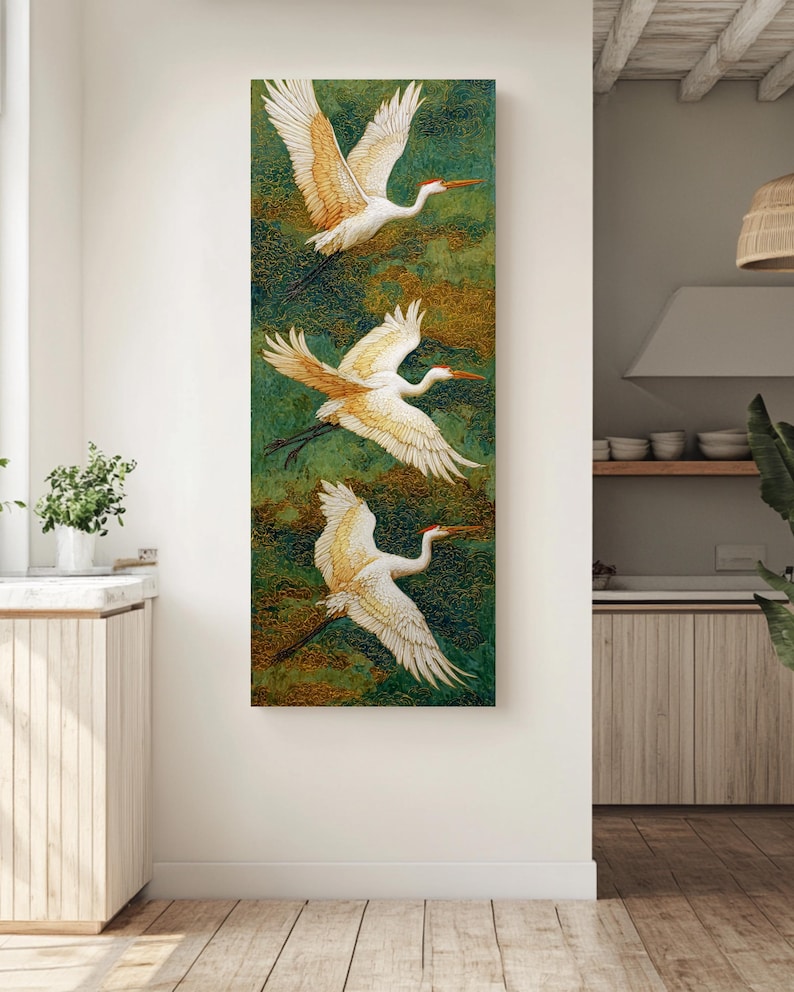 May include: A vertical canvas art piece featuring three white cranes in flight against a textured green and gold background. The cranes have outstretched wings with detailed feathering and orange beaks, creating a sense of movement and elegance. The artwork is displayed in a well-lit room.