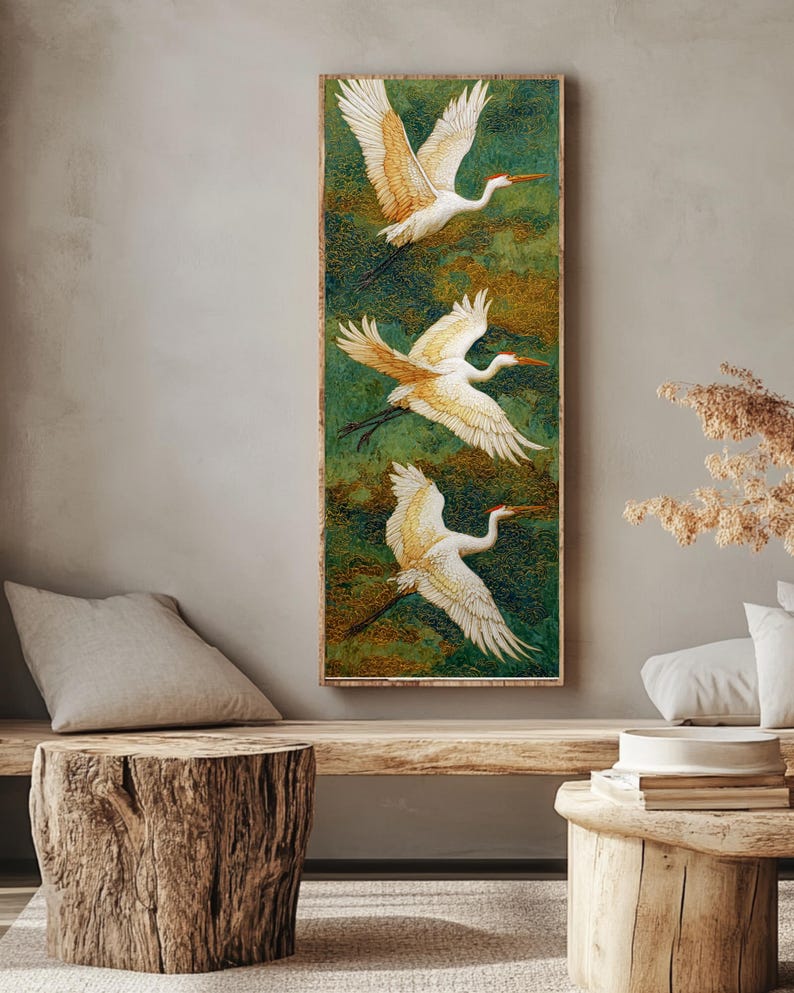 May include: A vertical rectangular artwork features three white cranes in flight against a green and gold background. The birds have outstretched wings and long legs. The artwork is framed in a light brown wooden frame, creating a serene and natural aesthetic.