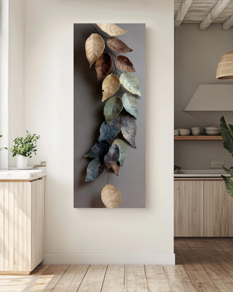 Op de afbeelding: Een verticaal kunstwerk voor aan de muur met een tak met meerdere bladeren in tinten beige, bruin en blauwgroen. De bladeren hebben een textuur en zijn geplaatst tegen een grijze achtergrond, wat een natuurlijk, decoratief element cre&euml;ert.