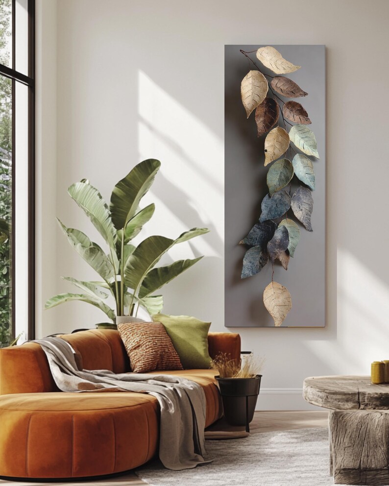 Op de afbeelding: Een moderne woonkamer met een oranje hoekbank, een grote plant in een pot en een houten bijzettafel. Een decoratieve wanddecoratie toont metalen bladeren in tinten bruin, goud en blauw. De kamer heeft een neutraal kleurenpalet.