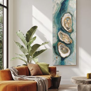 May include: An abstract wall art piece featuring three oyster shell designs in shades of white, gold, and teal. The artwork has a textured appearance and is set against a light blue and white background, creating a coastal theme.