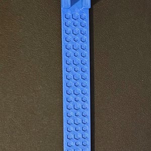 May include: A light blue, elongated, flat plastic tool featuring a repeating hexagonal honeycomb pattern along its length. The top end terminates in a V-shaped flared opening, while the bottom end is rounded. The surface has a matte finish.