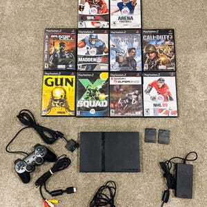 May include: A black PlayStation 2 console with one wired controller, power supply, AV cables, two memory cards, and ten game cases including titles like NHL 08, Madden NFL 07, Splinter Cell Pandora Tomorrow, Call of Duty 3, Gun, X-Squad, and TT Superbikes.