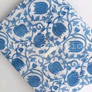 May include: White fabric with a repeating blue floral pattern. The design features stylized blue flowers and leaves connected by winding vines. The fabric is folded, showing the pattern's repeat. The text "Lucky Creation" is visible in the bottom left corner.