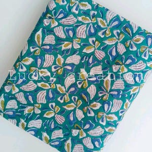 May include: Folded fabric featuring a teal background and a repeating floral pattern in white, blue, and yellow. The fabric has a tag that says "Lucky Creation".