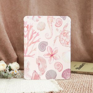 May include: A tablet case featuring a watercolor design of seashells, coral, a seahorse, and a turtle in shades of pink and gray on a light background. The case has a smooth finish and a rectangular shape.