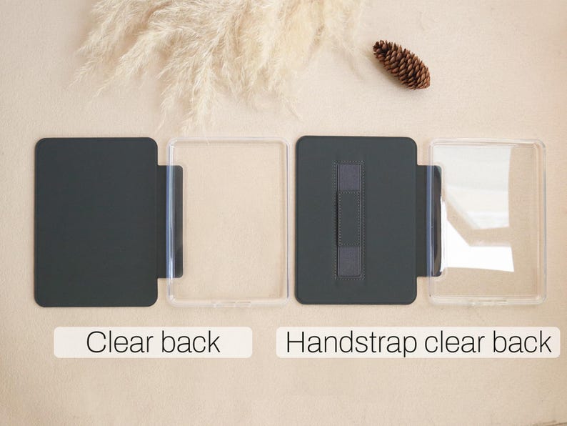 Puede incluir: Dos fundas transparentes para tel&eacute;fono con parte trasera gris oscuro, una con correa de mano. El texto "Clear back" y "Handstrap clear back" se muestra debajo. Una pi&ntilde;a y plantas secas en el fondo.