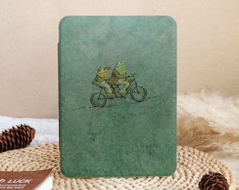 Puede incluir: Una funda verde para tableta con una ilustración de dos ranas en bicicleta. Las ranas llevan sombreros y chaquetas, sobre un fondo verde texturizado y moteado. La funda tiene esquinas redondeadas.