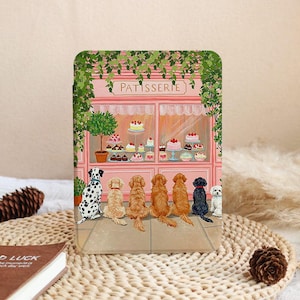 Peut inclure: Une coque de tablette rose avec une illustration d'une pâtisserie, présentant des gâteaux et des desserts. Une rangée de chiens de différentes races sont assis, observant la boutique. Le mot "PATISSERIE" est au-dessus de la fenêtre.