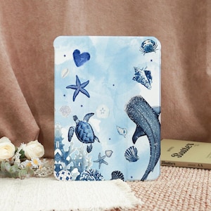 May include: A blue tablet case featuring an aquatic design. The case has illustrations of a whale shark, sea turtle, starfish, seashells, and coral against a light blue watercolor background. The case is rectangular and has rounded corners.