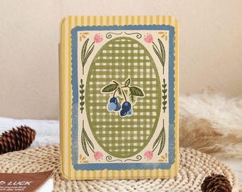 Puede incluir: Un diario decorativo con un borde a rayas amarillas y azules. El centro presenta un patrón de cuadros verdes con una ilustración de arándanos. Acentos florales rosas y un borde festoneado azul completan el diseño.