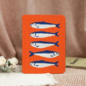 May include: An orange tablet case with a mosaic design of five blue and white fish. The fish are arranged vertically. The case is rectangular with rounded corners. The background is a textured orange. The case is likely for a tablet.