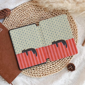 Puede incluir: Una funda negra para tableta con un dise&ntilde;o caprichoso. La funda presenta una secci&oacute;n a rayas rojas y rosas con dos ilustraciones de gatos negros. La parte superior tiene un patr&oacute;n floral repetitivo en verde y azul.