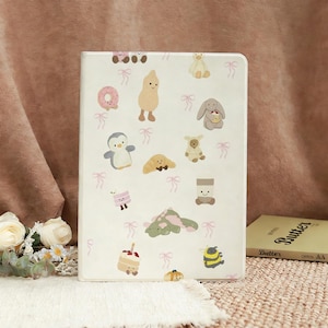 以下が含まれることがあります： ピーナッツ、ペンギン、クマなど、漫画の食べ物や動物のイラストが繰り返される白いタブレットケース。ピンクのリボンがデザイン全体に散りばめられています。ケースは長方形で、表面は滑らかです。