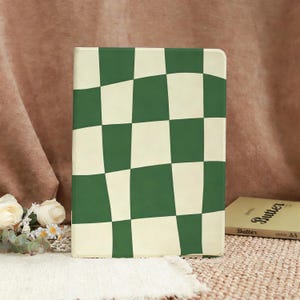 May include: A rectangular notebook with a green and cream checkered pattern. The notebook is standing upright on a beige surface. A book titled "Butter" is visible in the background.