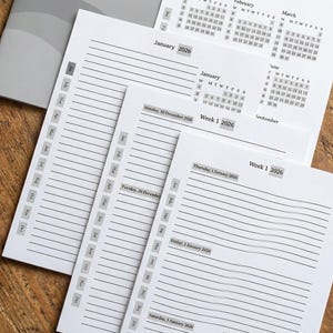 May include: A 2026 calendar and planner set. The cover is grey with the year printed in large black font. Inside, the planner pages are white with lined sections for each day, and a monthly calendar view.