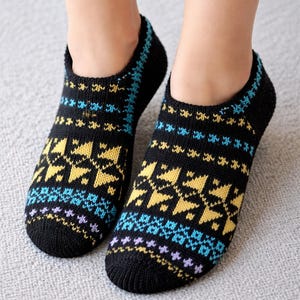 Puede incluir: Un par de calcetines negros de punto con un colorido estampado geométrico. El estampado incluye formas y líneas amarillas, azules y moradas. Los calcetines son tobilleros y parecen estar hechos de un material suave.