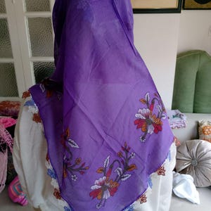 May include: A vibrant purple headscarf with floral patterns in red, orange, and white. The scarf features a delicate lace trim in white, blue, and brown. The head covering is made of a lightweight fabric.
