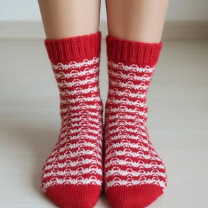 Op de afbeelding: Een paar rood-wit gestreepte sokken. De sokken hebben een rode boord, hiel en teen, met een wit golfpatroon op de schacht. De sokken zijn gemaakt van gebreid materiaal.